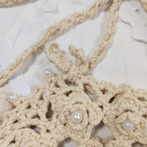 Close-up of beige crochet crossbody bag with hollow weave patterns and pearl bead accents