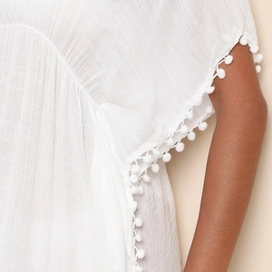 Détail du cache-maillot blanc avec bordure de pompons et tissu texturé et respirant