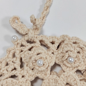Close-up of hand-crocheted hollow floral pattern with pearl bead and woven strap