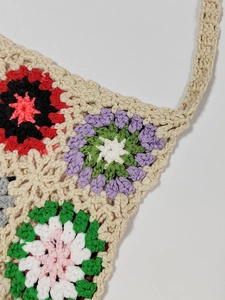 Detailed macro view of colorful crochet floral patterns on a beige woven fringe bag