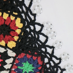Macro shot of colorful crochet pattern with handmade floral details and pearl beads