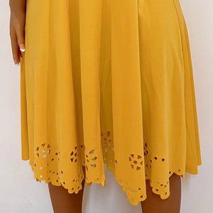 Detail of laser-cut floral pattern and scalloped hem on yellow short sleeve dress