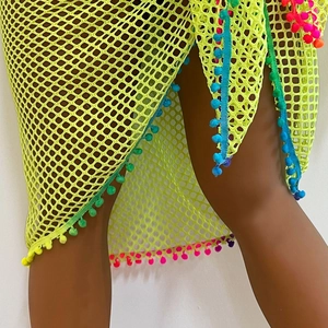 Detail of neon green mesh beach sarong featuring colorful pom-poms and a high side slit