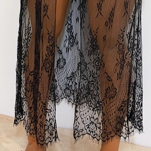Détail de la tunique en dentelle noire avec motifs floraux et ourlet à franges cils