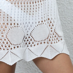 Detail of white crochet beach cover-up with hollow geometric patterns and scalloped hem