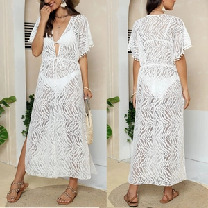 Detail of white lace beach cover-up with wavy patterns, pom-pom sleeves and front tie