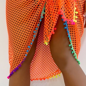 Close-up detail of orange mesh beach sarong featuring vibrant multi-colored pom-pom fringe trim