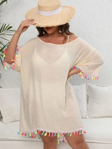 Détail des pompons colorés sur une tunique de plage crème avec fond texturé blanc