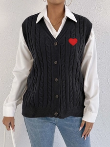 Detail of black cable-knit vest featuring a red heart patch and classic V-neck style