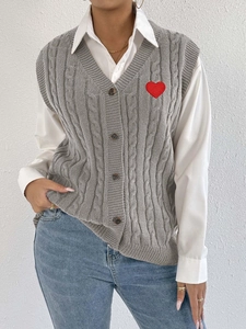 Detail of grey cable-knit vest featuring brown buttons and a red heart embroidery patch
