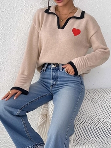 Close-up of beige knit polo sweater with black trim and red heart embroidery detail