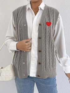 Close-up of cable knit grey vest featuring a vibrant red heart patch and classic brown buttons