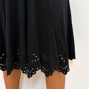 Close-up of the intricate laser-cut floral eyelet pattern on a black scallop hem dress