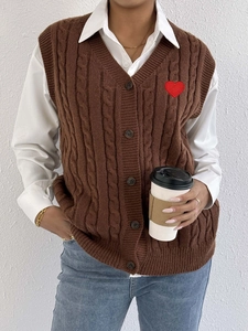 Detail of dark brown cable knit vest with red heart patch and button-up V-neckline