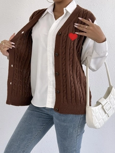 Detail of cable knit vest featuring a red heart embroidery patch and knit texture