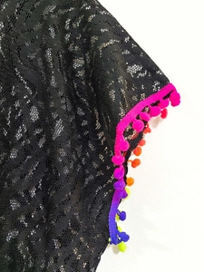 Dettaglio del copricostume in pizzo nero con pompon colorati e texture geometrica