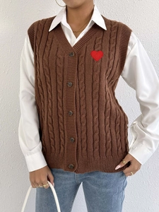 Close-up of brown cable knit vest with red heart embroidery and classic V-neck buttons