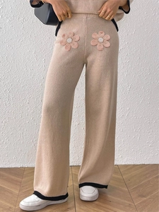 Dettaglio dei pantaloni in maglia beige con fiori rosa applicati e orli neri a contrasto