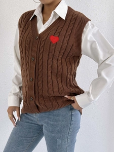 Close-up of brown cable-knit vest with red heart patch and V-neck button closure
