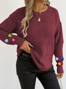 Detail of burgundy knitted sweater featuring colorful 3D crochet flowers on the sleeves
