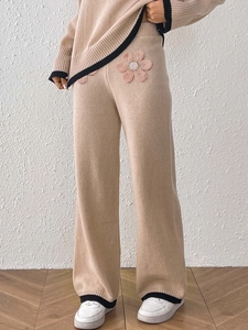 Dettaglio dei pantaloni in maglia beige con applicazione floreale e bordi a contrasto