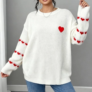 Close-up of white knit sweater featuring red heart embroidery and textured fabric