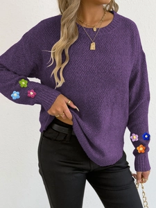 Close-up of colorful 3D crochet flowers on dark purple knit sweater sleeves
