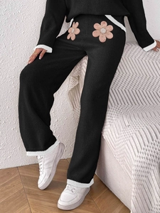 Dettagli di fiori rosa con perle su pantaloni in maglia nera a gamba larga con bordi bianchi