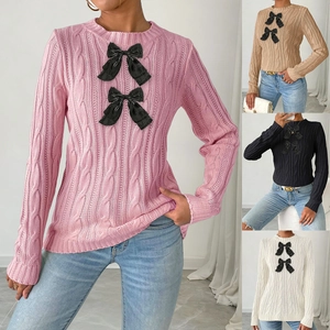 Detail of cable knit pattern and decorative black bows on a long-sleeve crewneck sweater