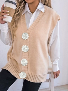 Detail of knit vest featuring 3D floral buttons and soft ribbed texture on beige fabric