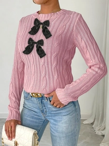 Detail of pink cable knit sweater with elegant black bow accents and crew neck style