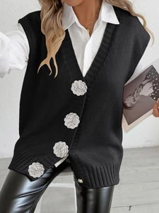 Detail of black knit vest featuring 3D white floral buttons and vertical ribbed texture