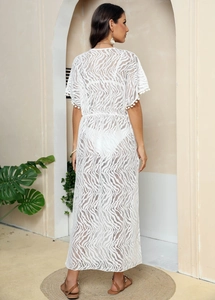 Detail of white lace beach cover-up featuring pom-pom trim and sheer zebra pattern