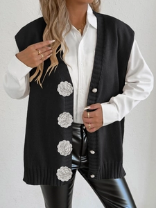 Detail of knit vest featuring 3D white crochet flowers and elegant pearl buttons on black fabric