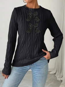 Detail of cable knit black sweater featuring glossy bow accents and ribbed crew neck finish