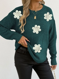 Detail of 3D white floral applique and beadwork on dark green knit sweater