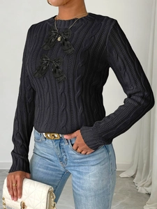 Detail of black cable knit sweater featuring decorative bow accents and round neckline