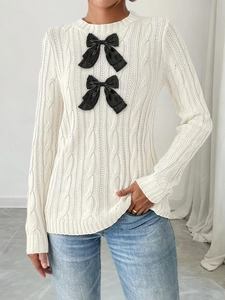 Close-up of white cable knit sweater featuring large black decorative bows and ribbed cuffs