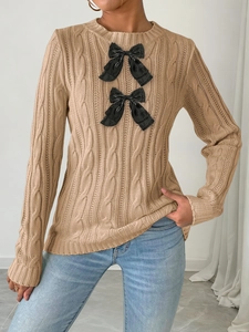 Detail of camel knit sweater with cable pattern and two decorative black bows on the front