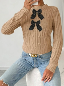 Detail of beige cable knit sweater featuring 3D black bows and classic crew neck