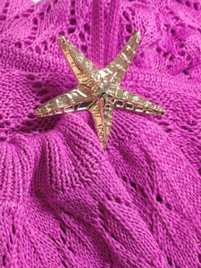 Détail de l'accessoire en forme d'étoile de mer dorée sur une robe en crochet rose