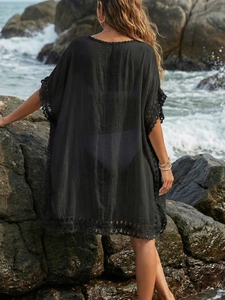 Back view of a loose black beach cover-up with crochet lace trim on a rocky seaside background