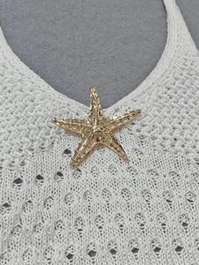 Detailed macro view of a golden metal starfish accessory on a white knit beach dress