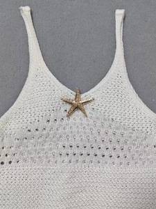 Close-up of white crochet beach dress featuring a gold starfish metal ornament