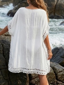 Back view of a white crochet trim beach cover-up against a scenic ocean and rocky coast