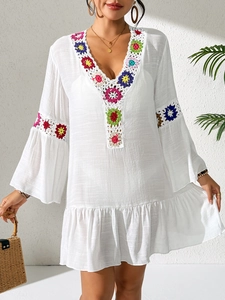 Detail of white beach dress featuring colorful handmade crochet floral patches and V-neck