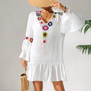 Detailed close-up of colorful handmade crochet floral patchwork on a white bohemian beach dress