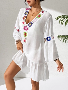 Close-up detail of colorful crochet floral patterns on white bohemian beach dress sleeve