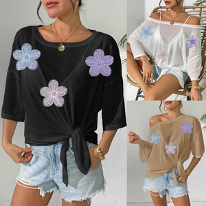 Detail of loose women's blouse featuring colorful 3D floral mesh appliques and side knot hem