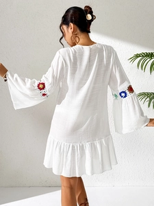 Detail of bohemian white dress showing colorful crochet flower sleeve and ruffled hemline